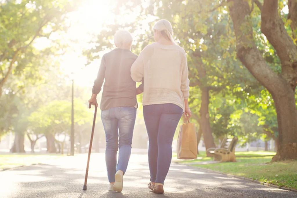 Adult daughter walking outdoors with an older woman using a cane