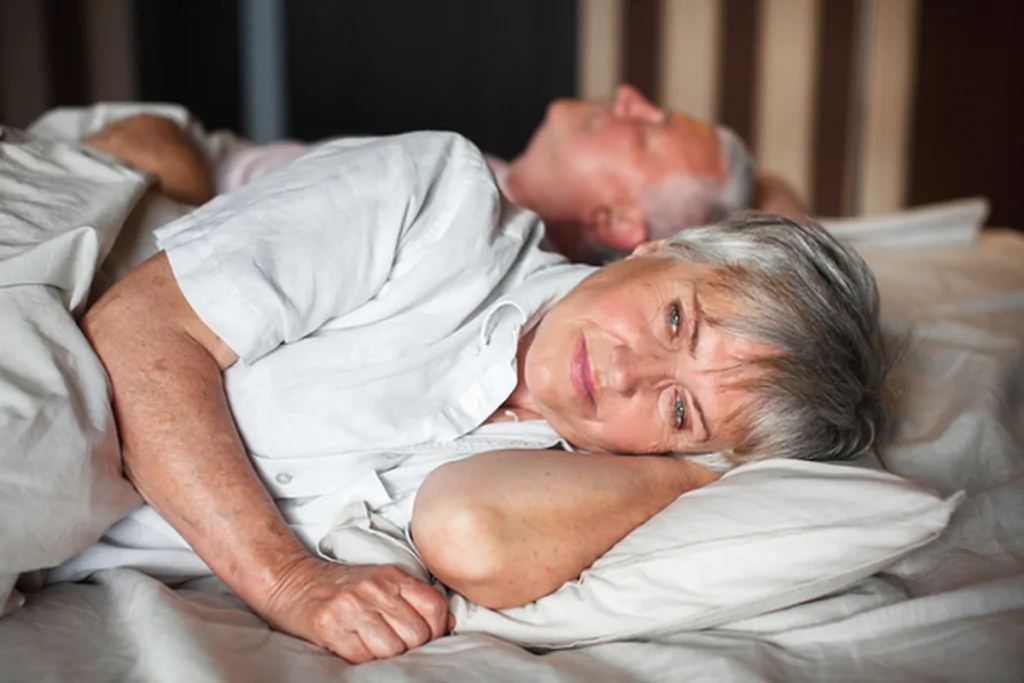 Older woman lying awake in bed looking unwell