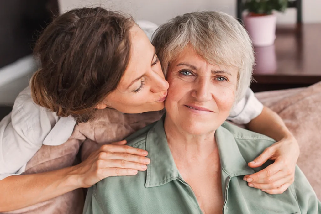 Adult daughter kissing her mother on the cheek at home