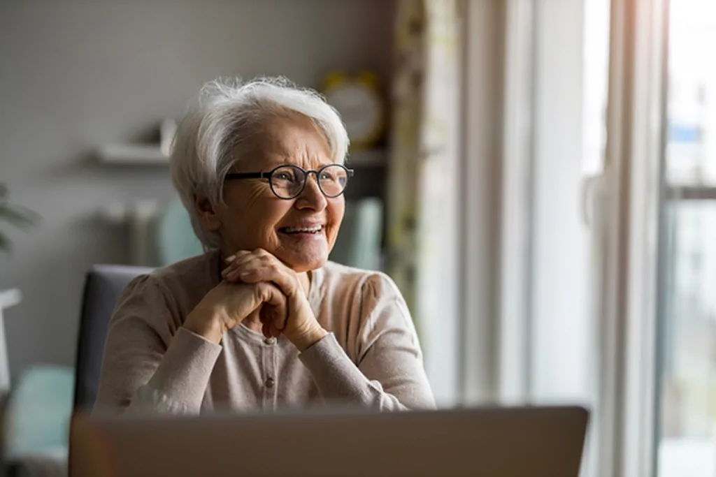 Older woman smiling at a laptop in her own living room