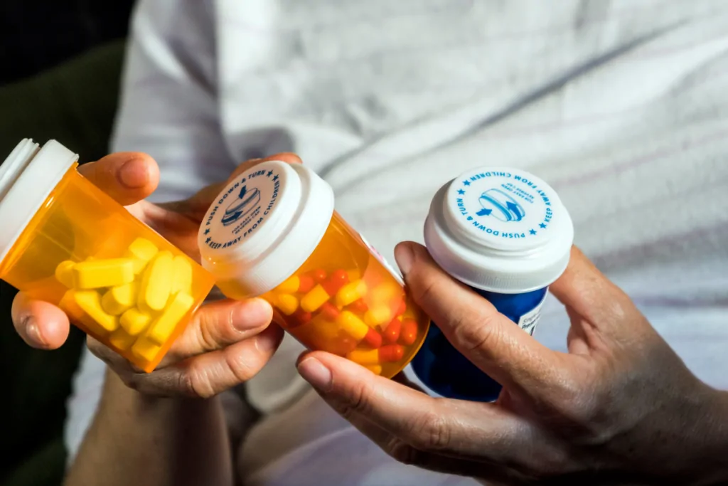 Hands holding several prescription pill bottles