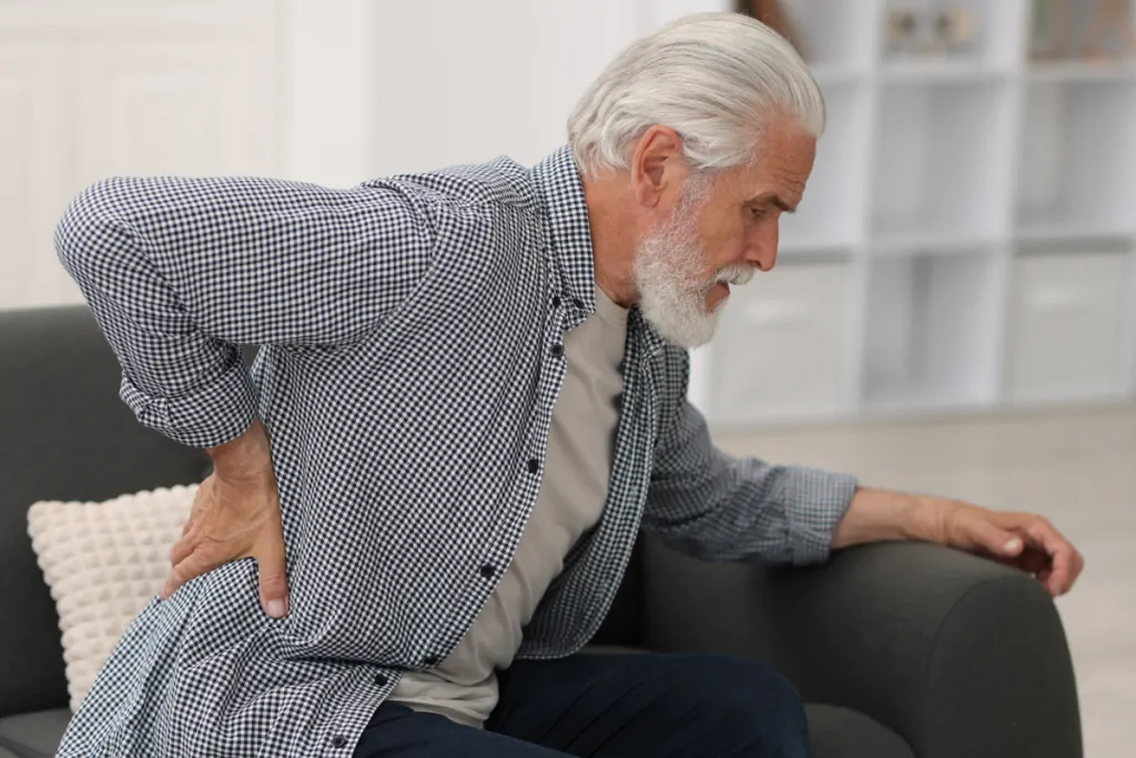 Older man sitting on a sofa holding his lower back in pain